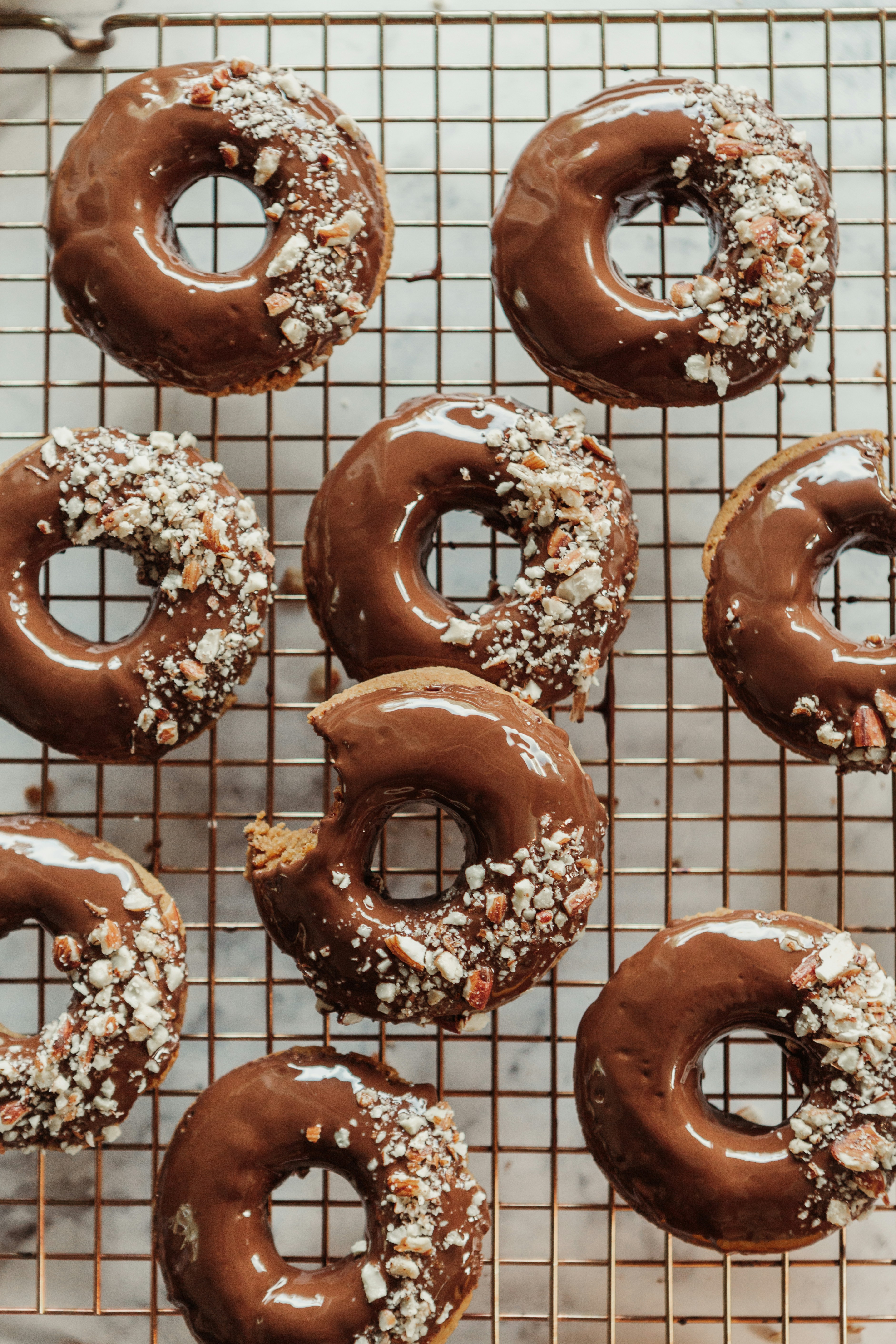 Chocolate-glazed donuts with nuts on a copper cooling rack