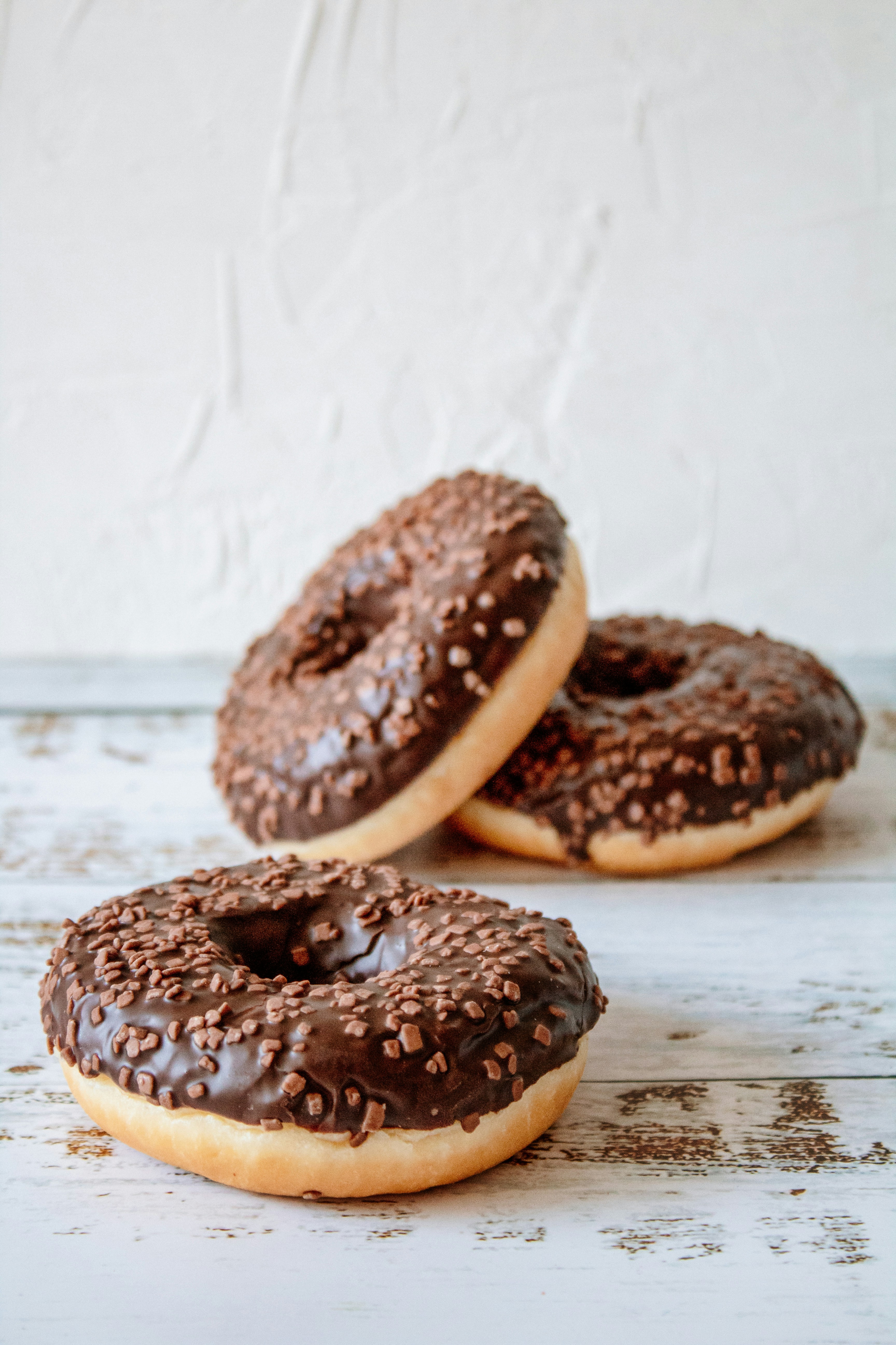 Chocolate-glazed donuts topped with chocolate sprinkles on a white surface
