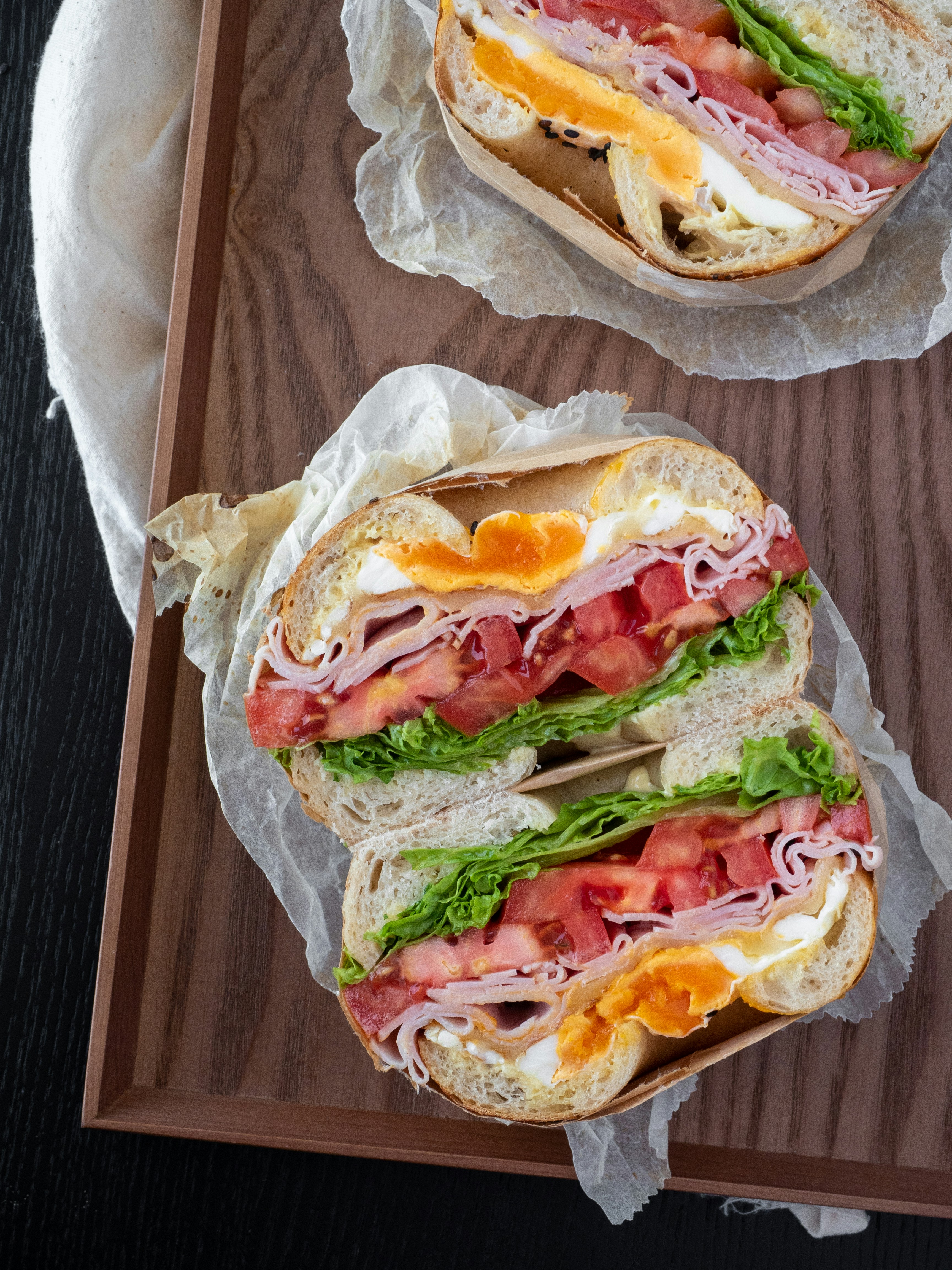 Bagel sandwich with egg, ham, tomato, and lettuce on a wooden tray