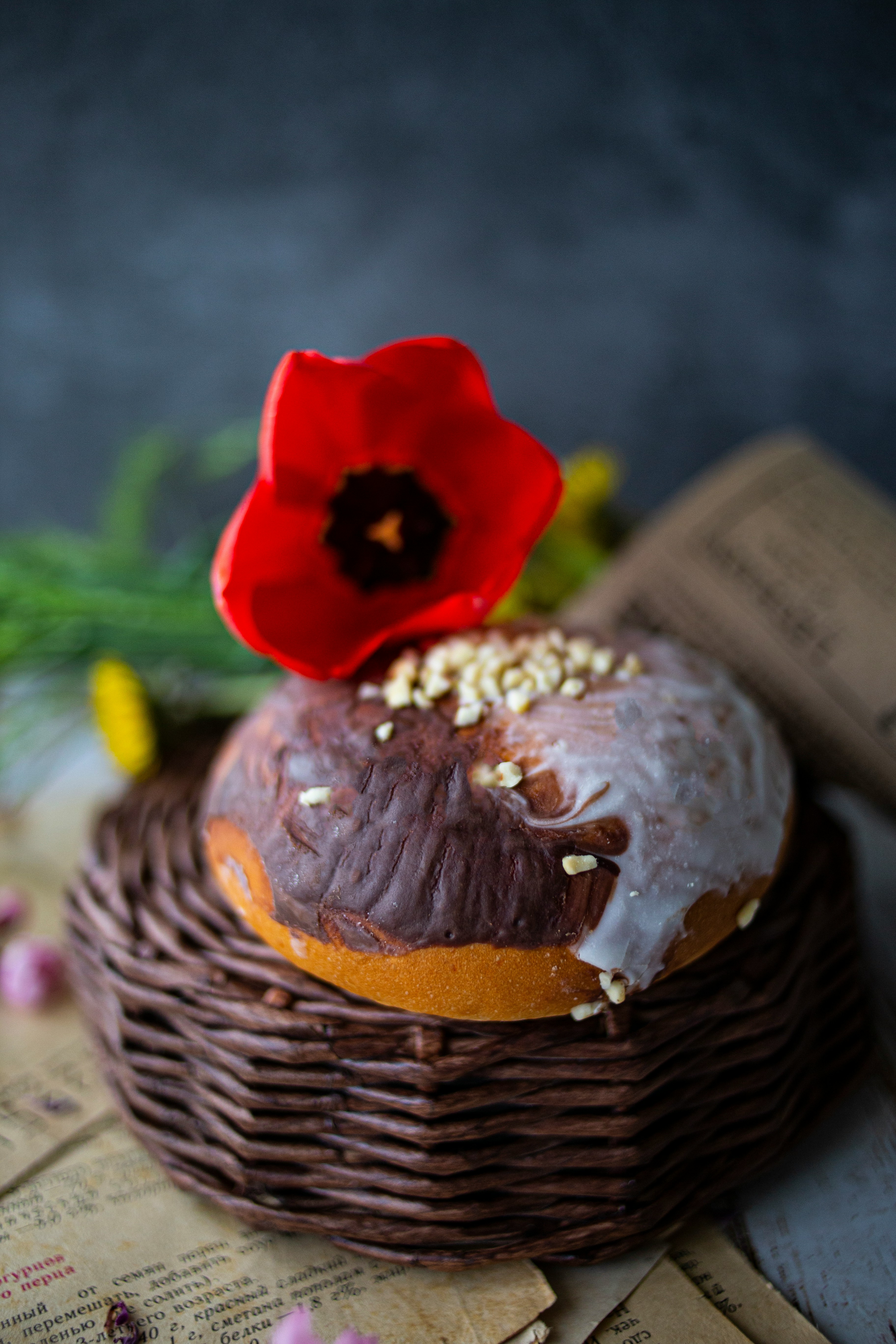 Glazed pastry topped with a red flower on a woven stand